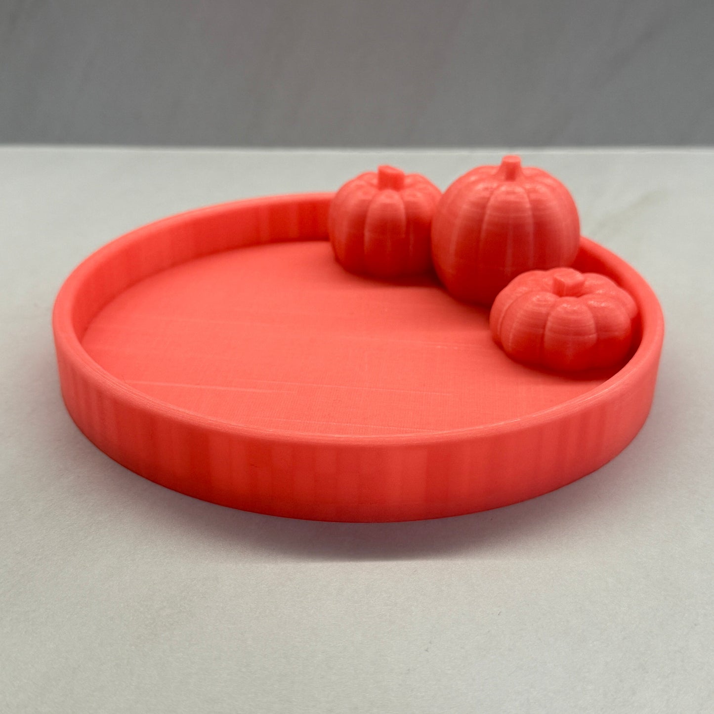 Coral-colored soap dish with three pumpkins on a light gray background