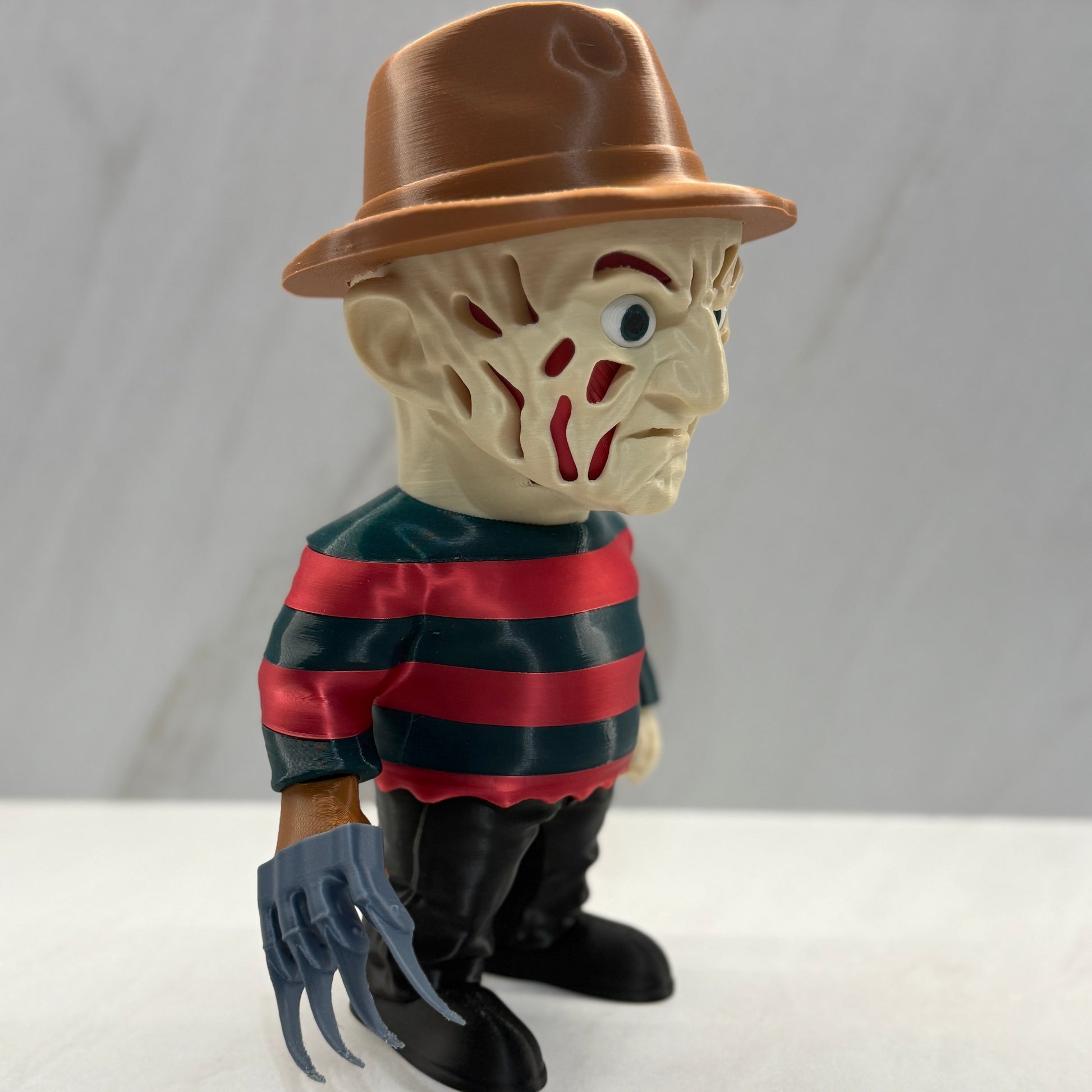 Toy figure of a character with a brown hat, striped shirt, and clawed gloves on a white background