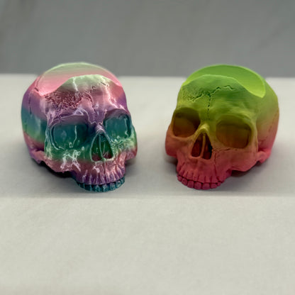 Two colorful skull-shaped objects on a white surface with a gray background