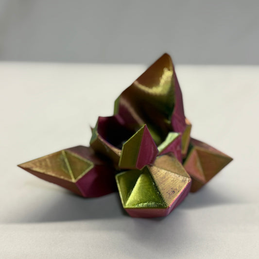Geometric metallic object with gold and purple colors on a white surface