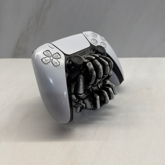 White gaming controller with black mechanical claw attachment on a gray background Bane controller holder batman