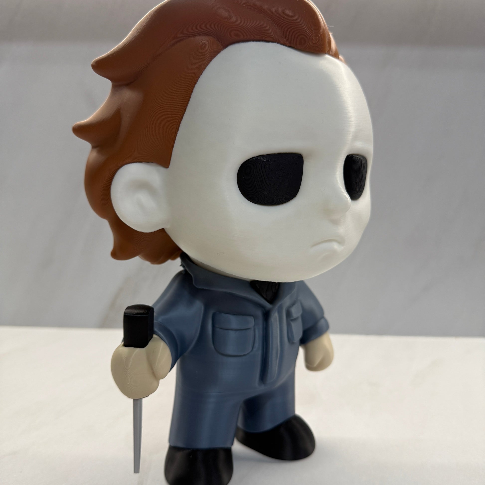 Toy figure of a character with a white face, brown ears, and blue outfit on a plain background