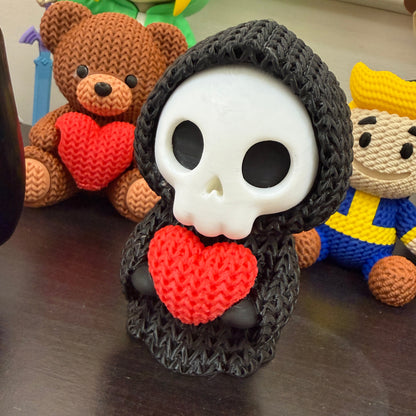 Crocheted skull with red heart surrounded by small figurines on a reflective surface