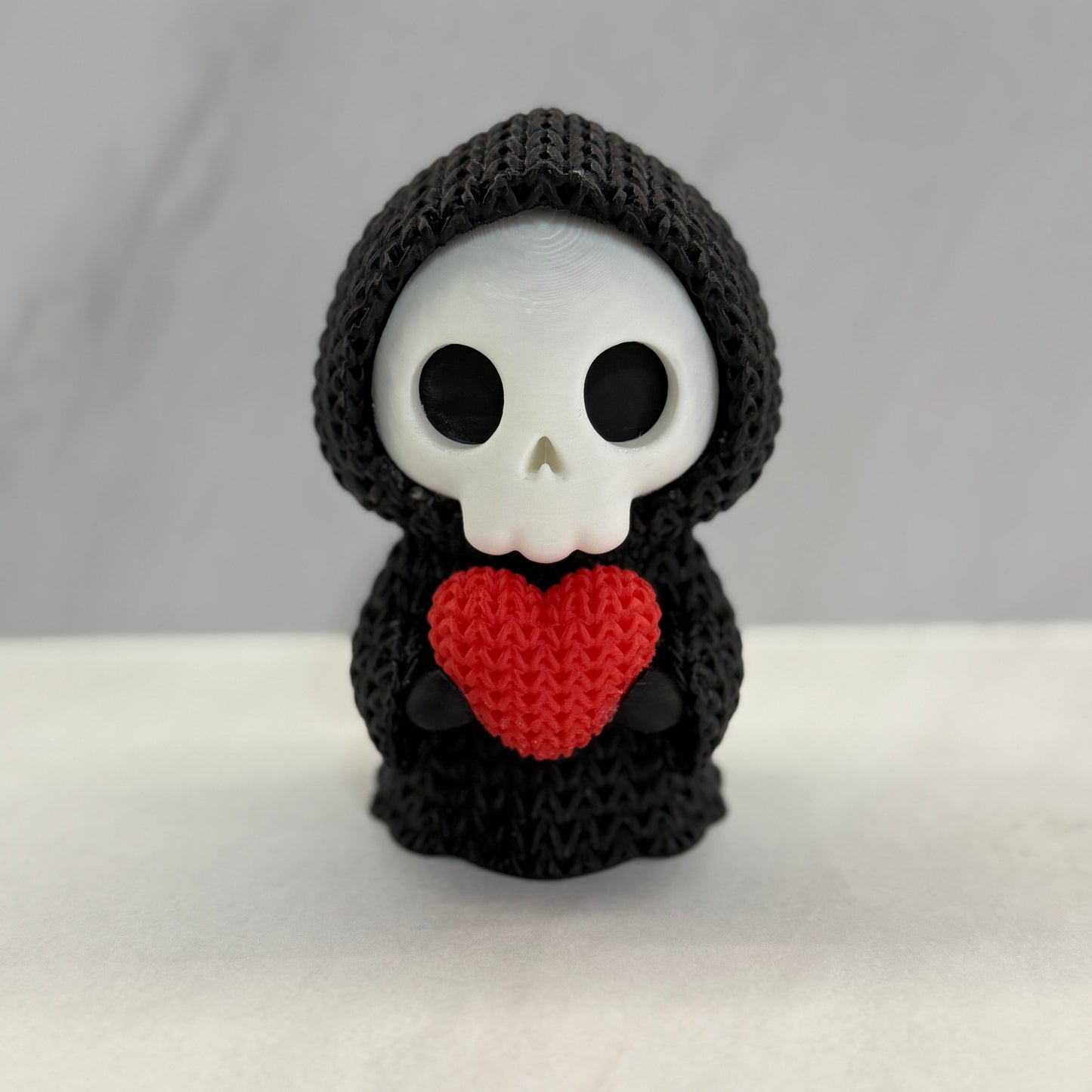 Crocheted skeleton toy with a red heart on a white background